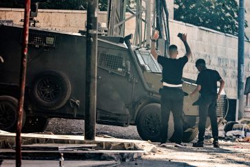 A Palestinian youth lifts his arms as he stands in front of an Israeli armoured vehicle in Jenin in the occupied West Bank on September 4, 2024, during an ongoing military raid. Israeli forces have killed at least 30 Palestinians across the northern West Bank since August 28, the territory's health ministry says, while Israel's military reported one soldier killed in the "counter-terrorism" raids. (Photo by Zain JAAFAR / AFP)